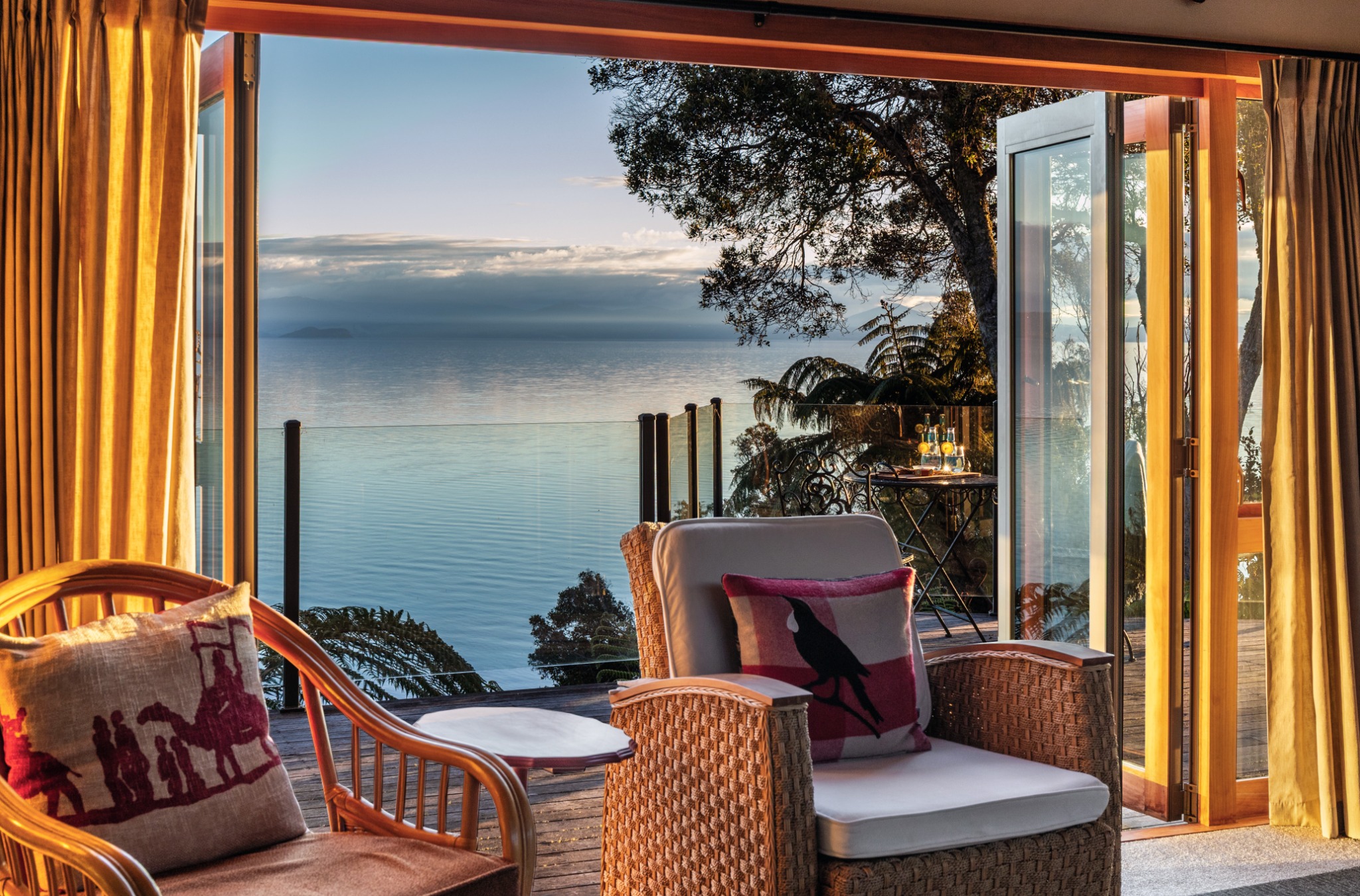 Golden light inside the lodge, wicker chairs and open doors looking onto Lake Taupō